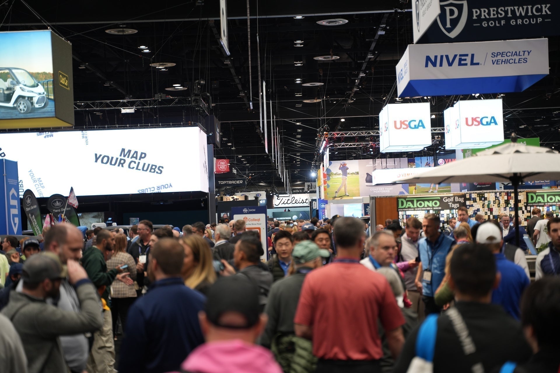 The 2025 PGA Show product display floor with many golf brand logo signs and patrons walking among the displays