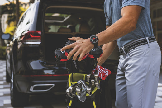 A golfer wearing a Garmin Approach S70 golf watch as he pulls his golf bag out of the rear of his SUV