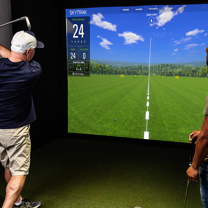 Two men, one swinging a golf club, in a home golf simulator with SkyTrak software on the impact screen in front of them