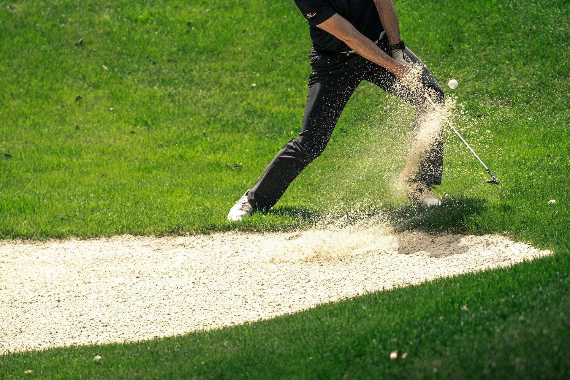 A golfer hitting golf ball and sand out of a golf course bunker on a sunny day