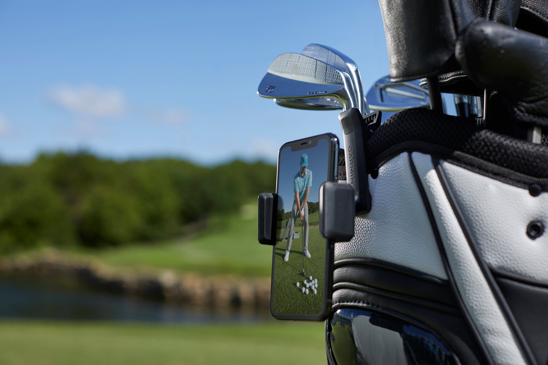 The Garmin Golf app on a smartphone clipped to a golf bag showing video of a golfer from front view getting ready to swing