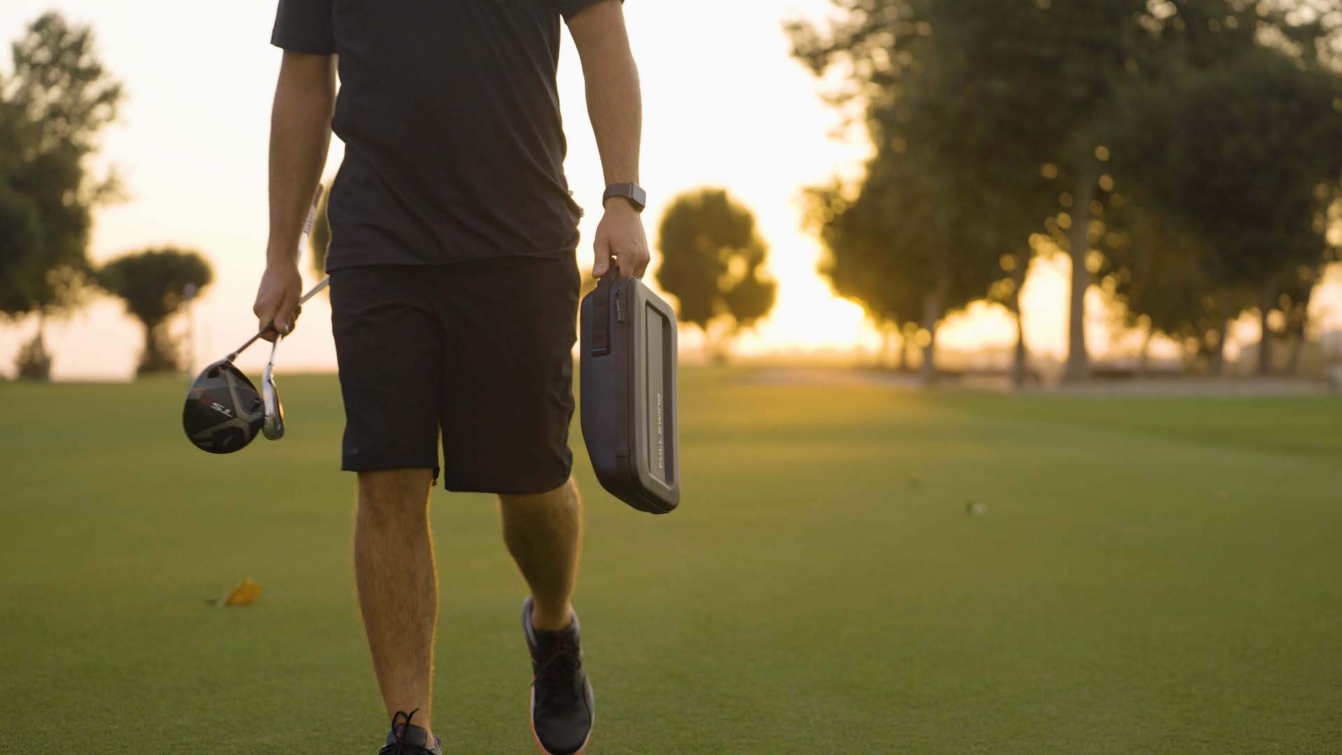 Golfer carrying Full Swing KIT in the carrying case and a golf club across the golf course