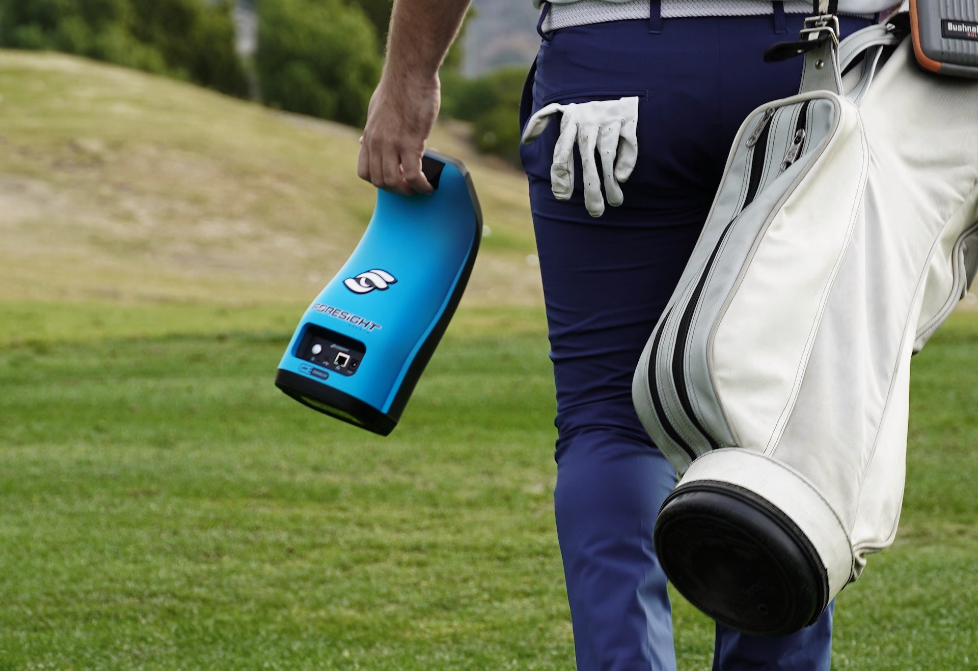 A golfer walking away with his golf bag and a Garmin GC3S launch monitor in the other hand