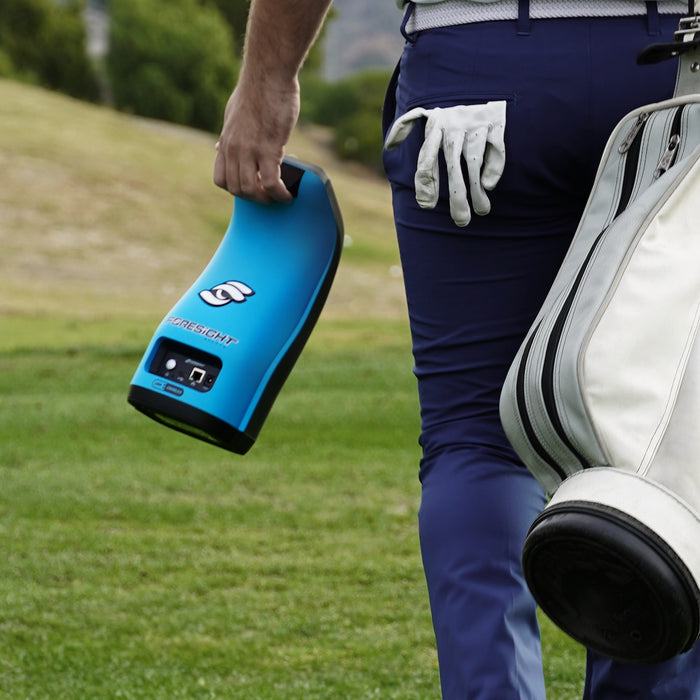 A golfer walking away with his golf bag and a Garmin GC3S launch monitor in the other hand