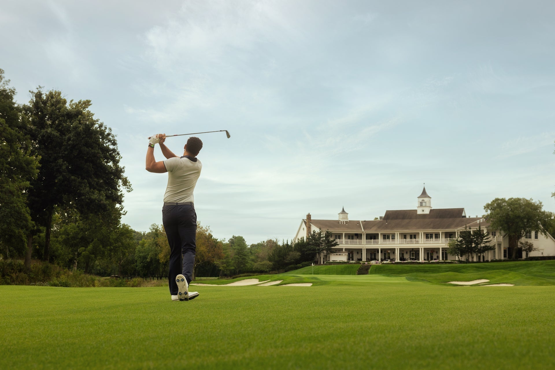 Golfer post swing on a golf course with the clubhouse in the foreground