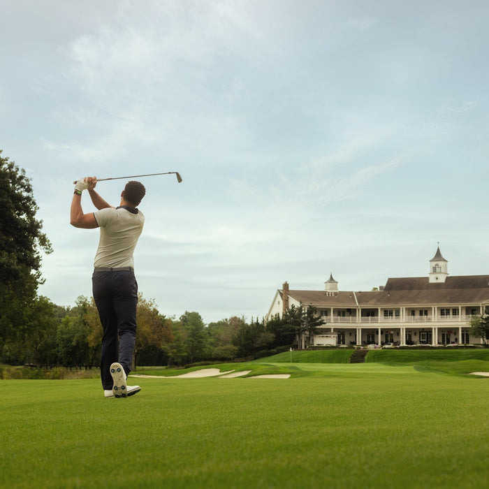 Golfer post swing on a golf course with the clubhouse in the foreground