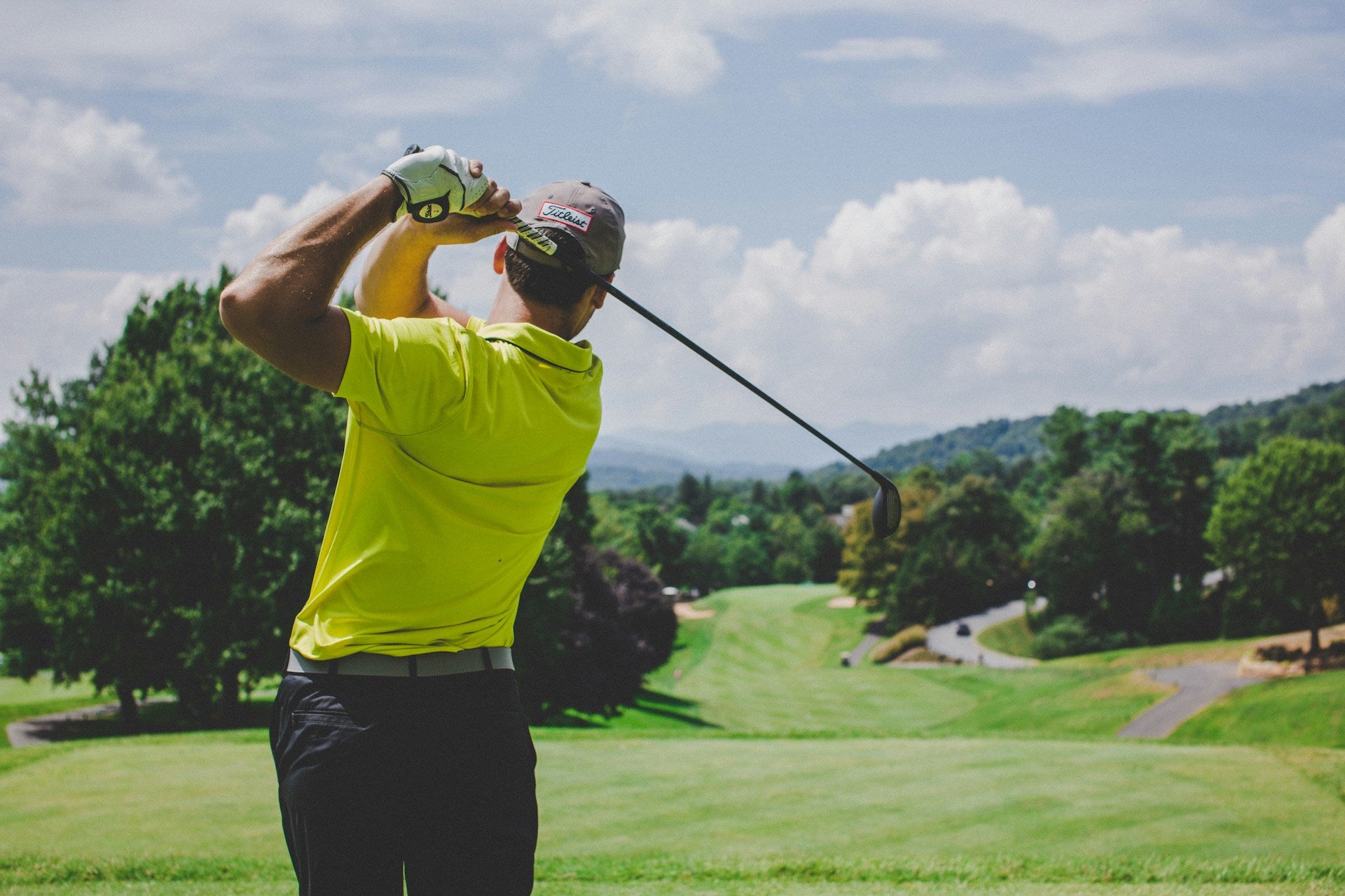 Golfer in a yellow shirt post-swing still looking out at his shot down the fairway on a bright golf course