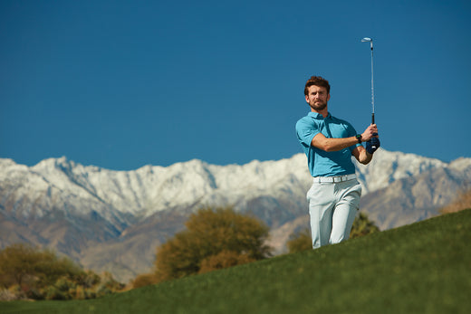 A golfer with a club post-swing on a golf course with a mountain range behind him