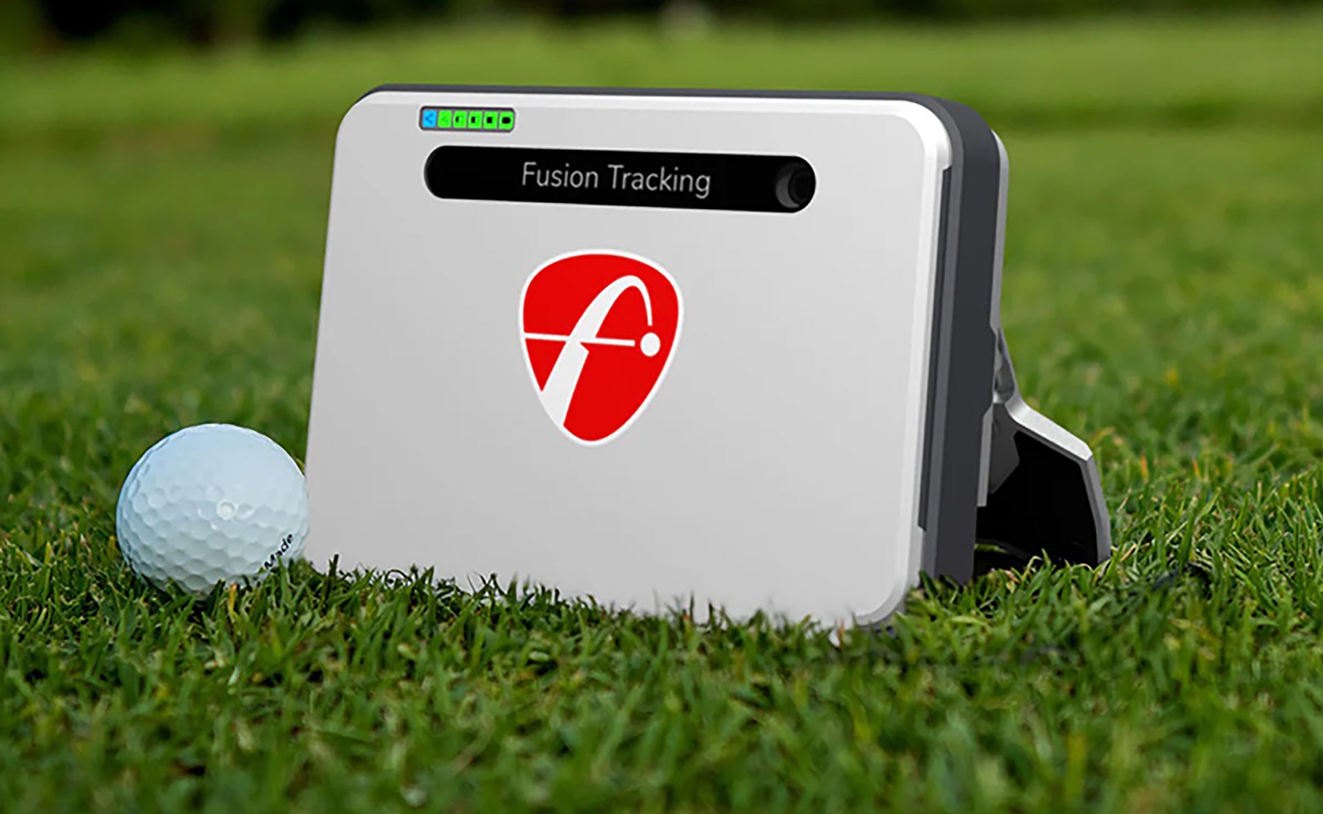 The 2024 FlightScope Mevo+ sitting on the golf course with a golf ball next to it