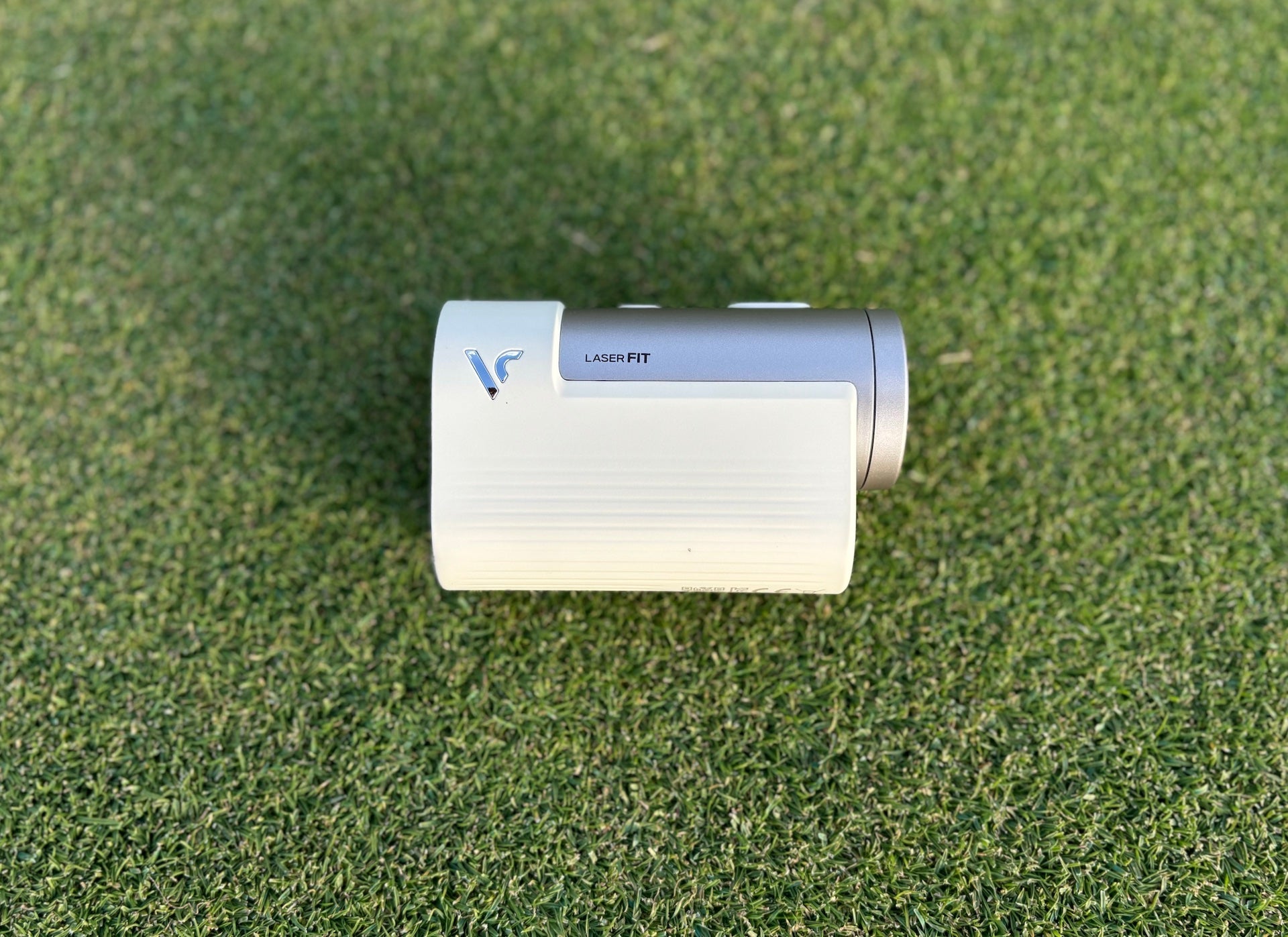 The Voice Caddie Laser FIT golf rangefinder sitting on its side on a golf hitting mat