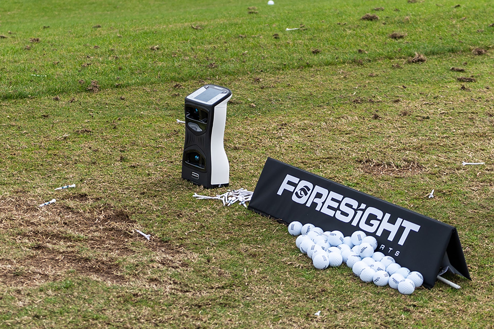 The Foresight Sports QuadMAX on the driving range next to a Foresight sign and a bunch of golf balls