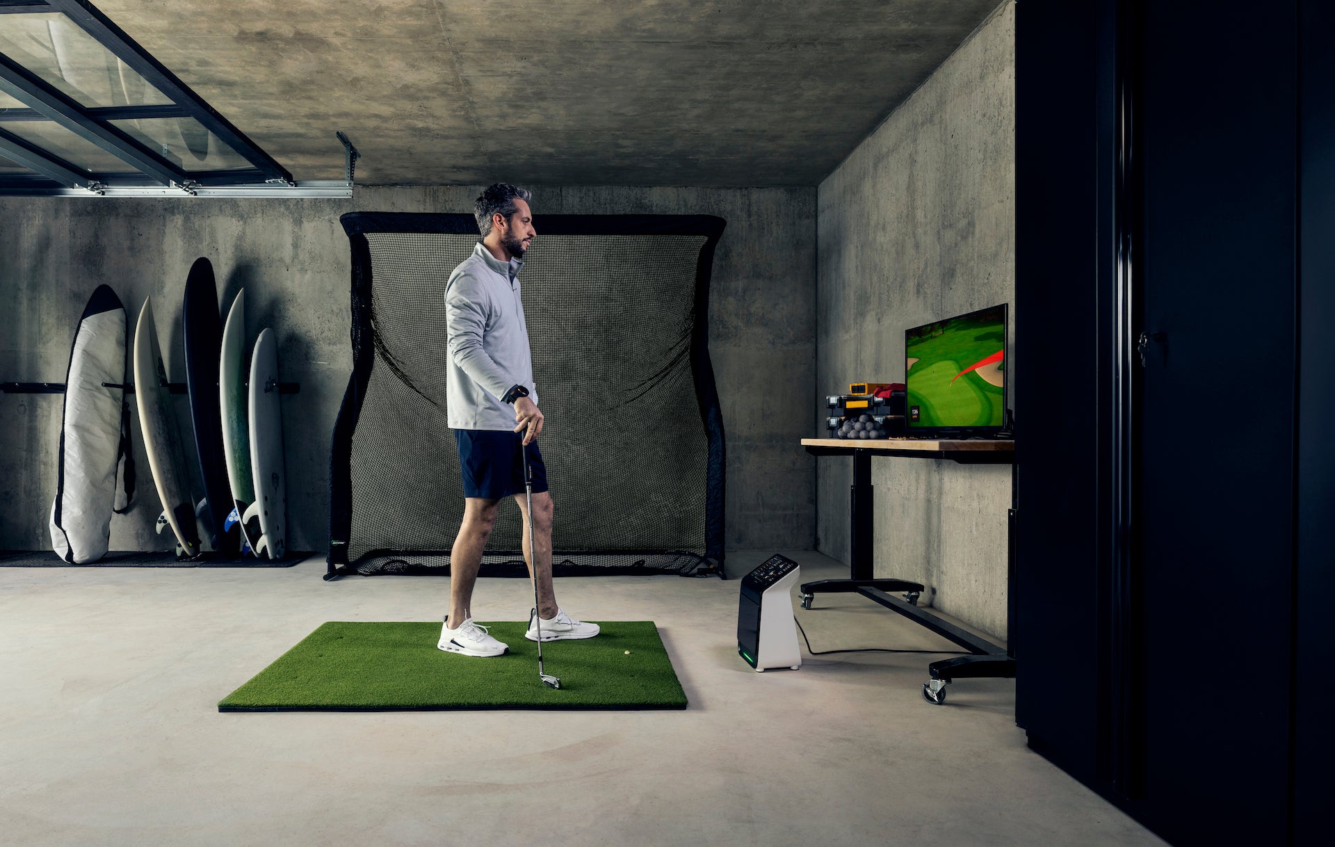 Golfer in a garage golf simulator with the Garmin Approach R50, golf hitting mat, and a golf hitting net