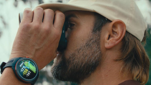 A golfer with hand to his eye with a golf rangefinder wearing a Garmin Approach S70 golf watch on his wrist