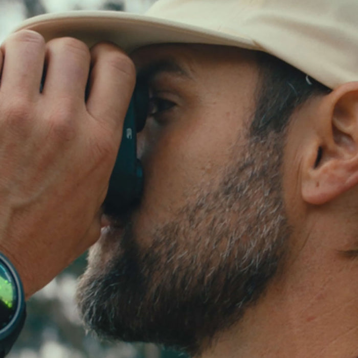 A golfer with hand to his eye with a golf rangefinder wearing a Garmin Approach S70 golf watch on his wrist