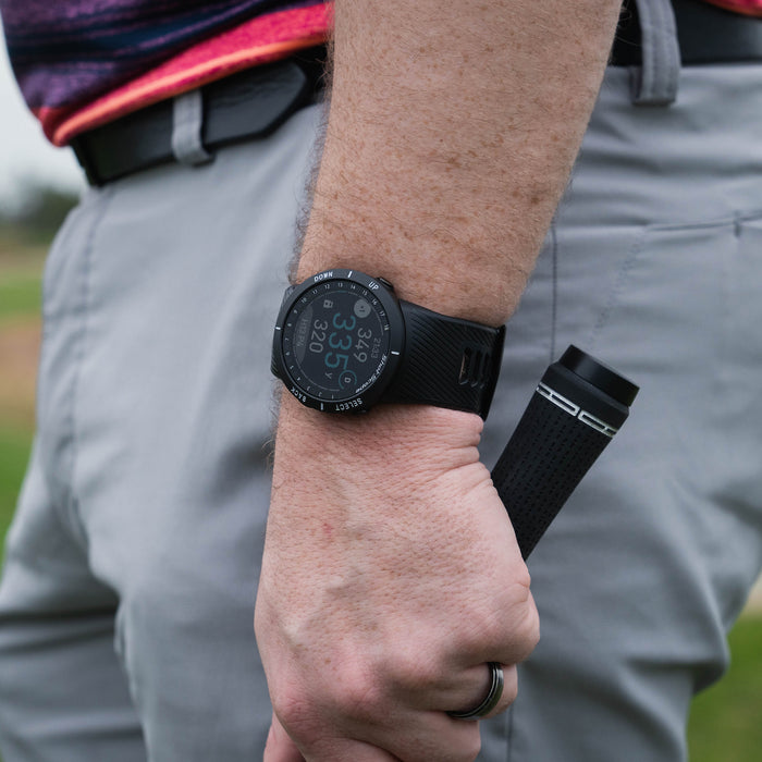 A Shot Scope V5 golf watch on a golfer's wrist while he's holding a golf club with a Shot Scope club tracker on it