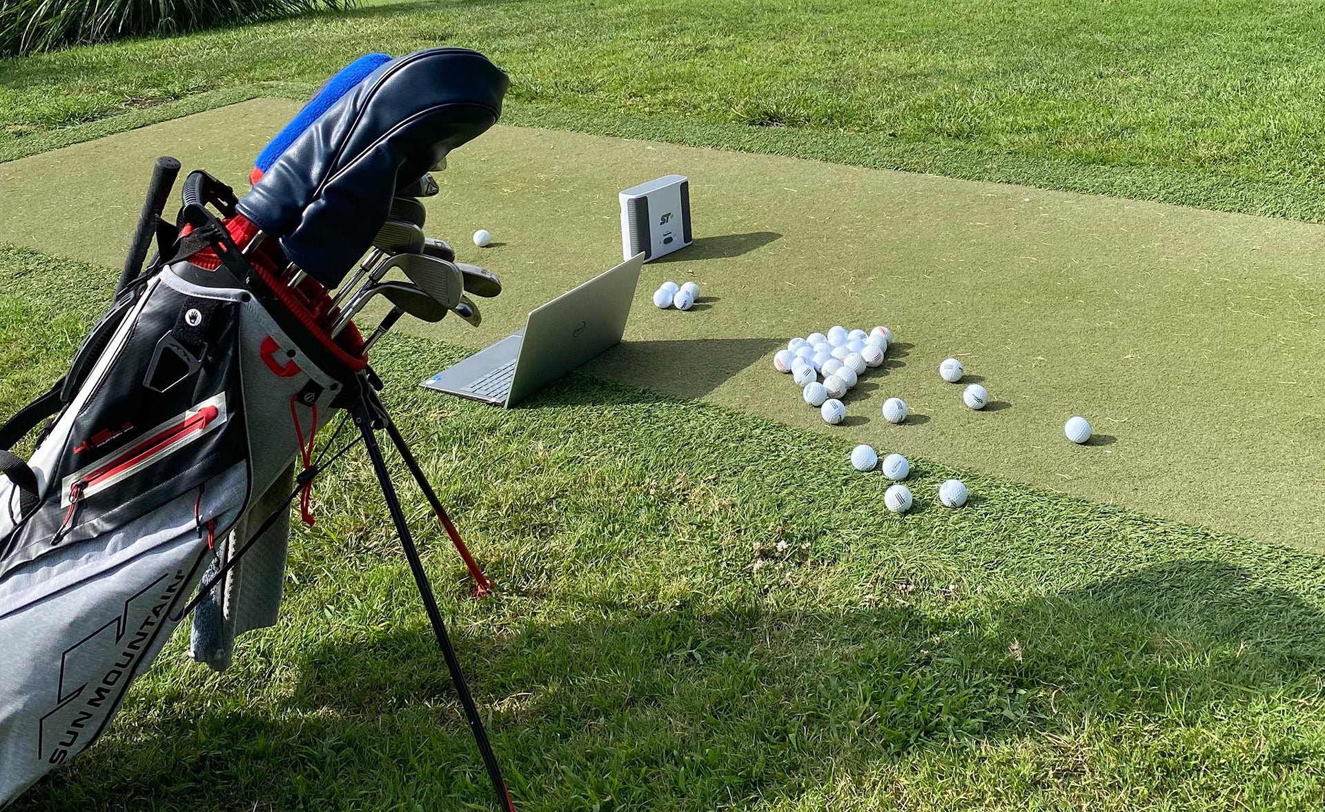 The SkyTrak+ at the golf range with a laptop, golf bag and many golf balls (image by PlayBetter golf reviewer Marc)