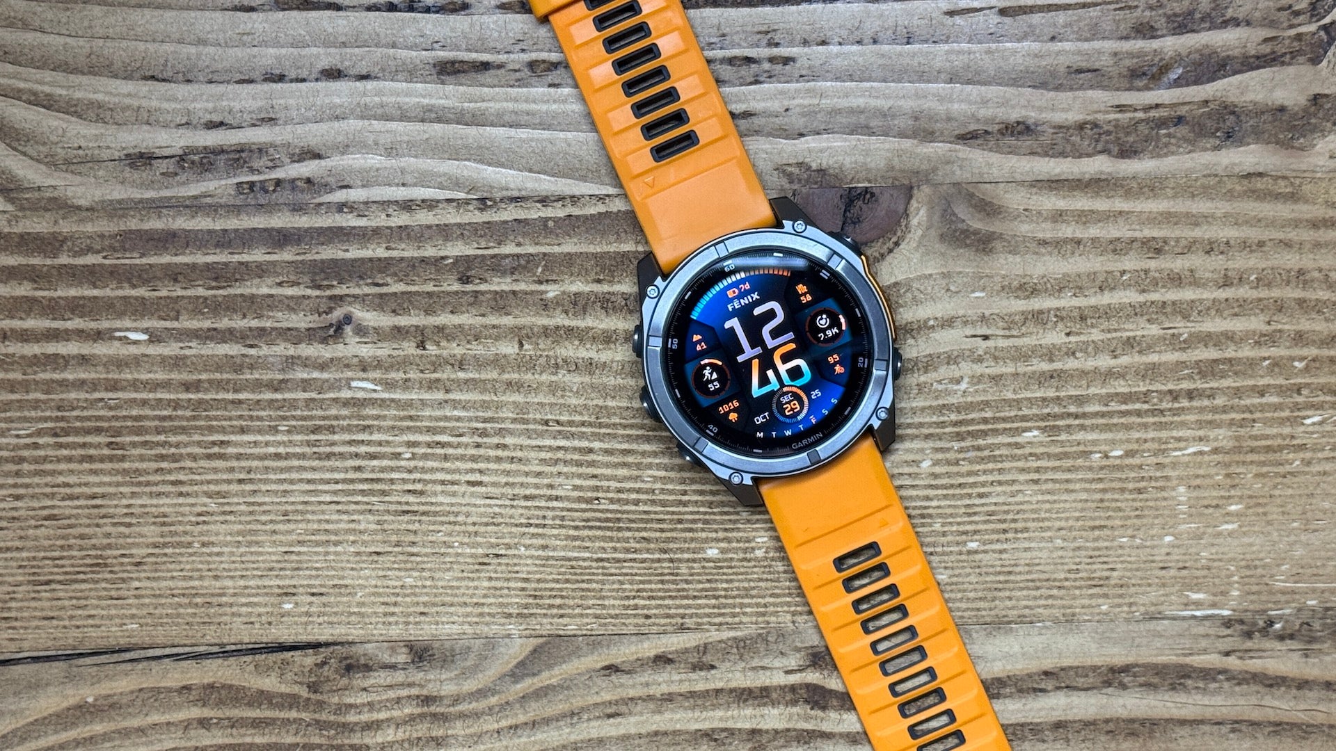 The orange 51 mm Garmin fenix 8 AMOLED multisport watch laying flat on wood 