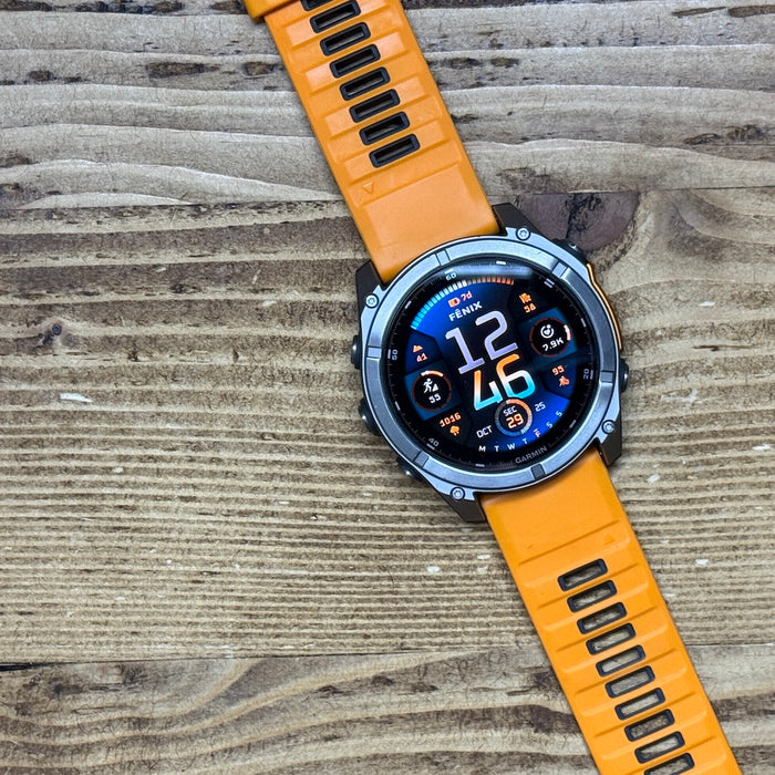 The orange 51 mm Garmin fenix 8 AMOLED multisport watch laying flat on wood 