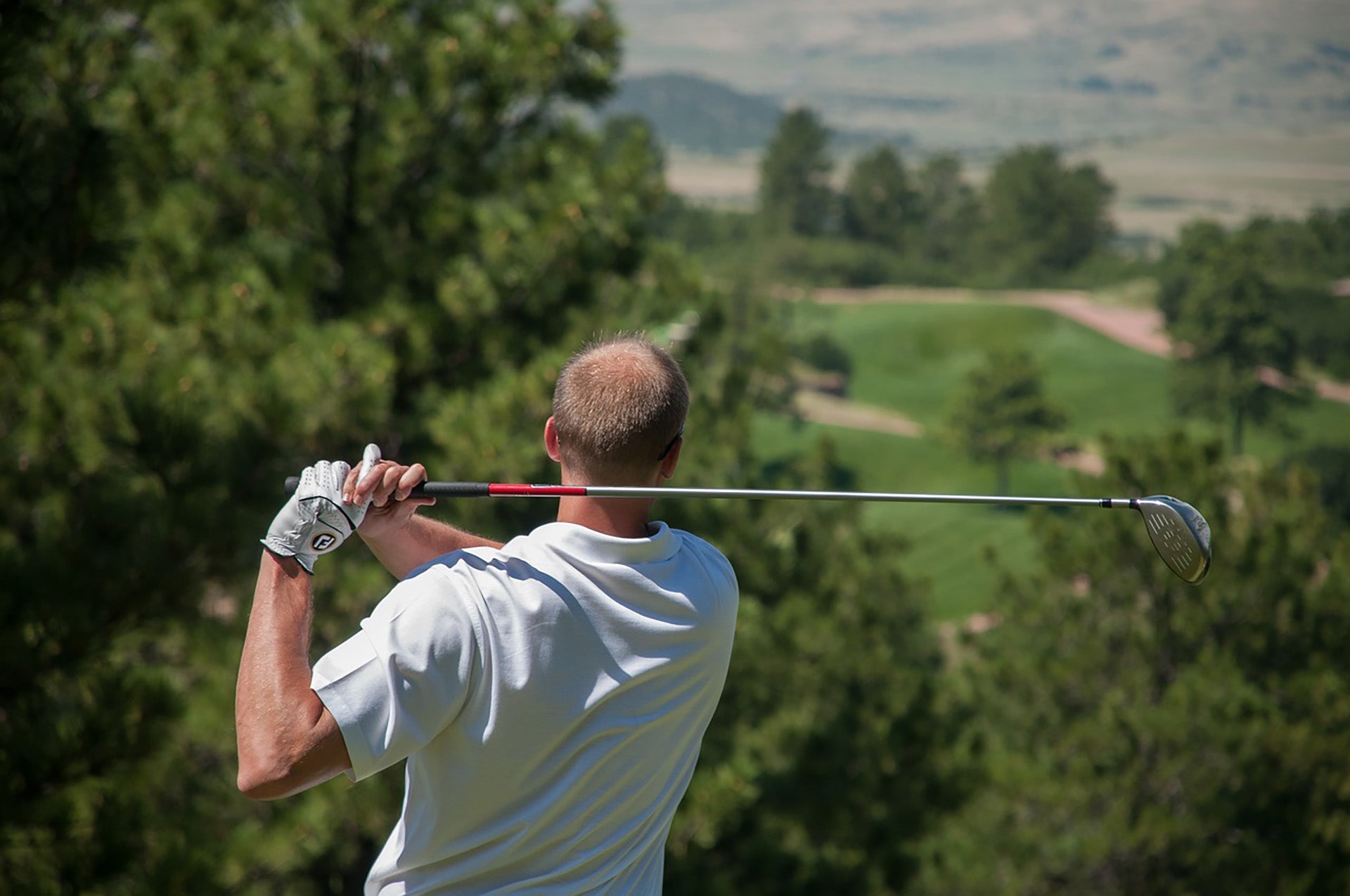 A golfer post swing looking out over a valley of a golf course