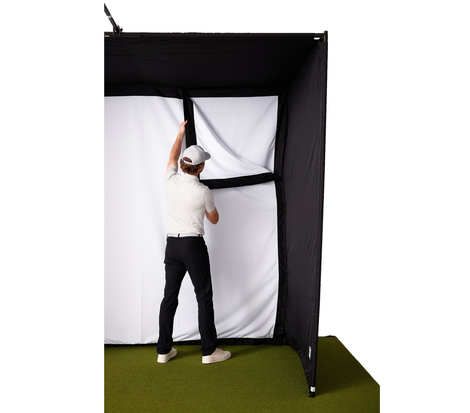 A man attaching the golf impact screen to the enclosure of the PlayBetter SimStudio golf simulator sitting on a golf hitting mat and landing turf